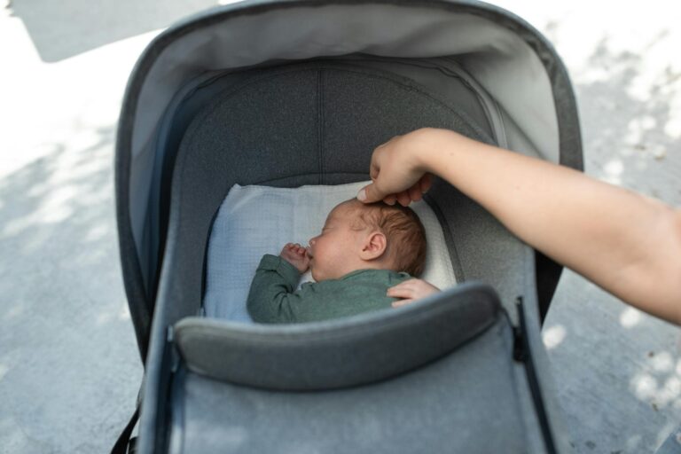 A serene moment of a baby sleeping in a stroller with a gentle touch from an adult hand.